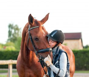 Young teenage girl equestrian kissing her chestnut horse. Multicolored outdoors horizontal image.